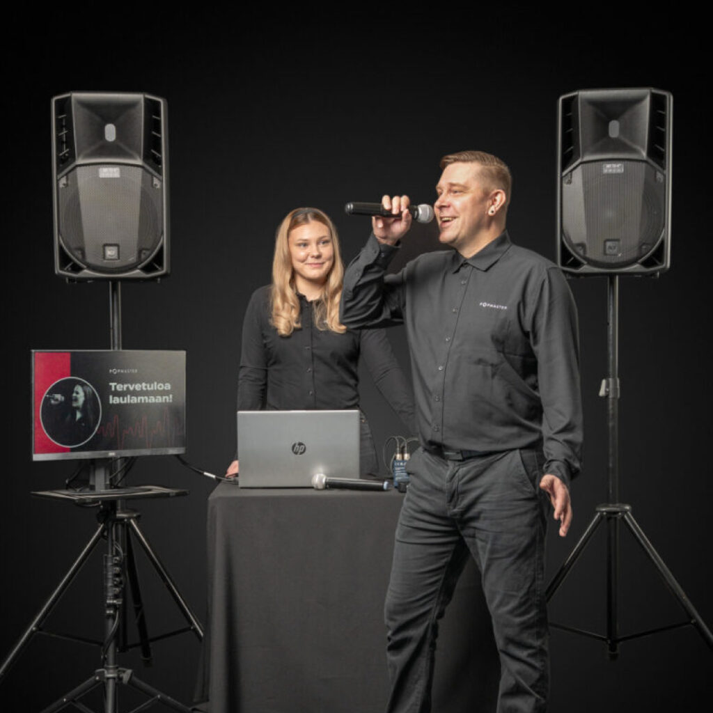 DJ ja karaokejuontaja esiintymässä Popmasterin Peruspaketin ammattilaisella äänentoistolla, taustalla kaiuttimet, tietokone ja laulunäyttö – DJ Vaasa ja lähialueet juhliin, yritystapahtumiin ja häihin.